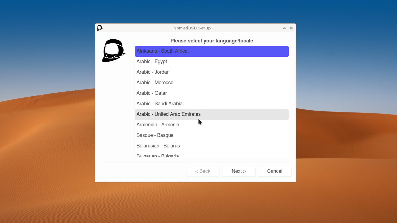 Jendela NomadBSD Setup meminta memilih bahasa/locale dari daftar seperti Afrikaans, Arabic, Armenian, Basque, dengan latar belakang wallpaper gurun pasir