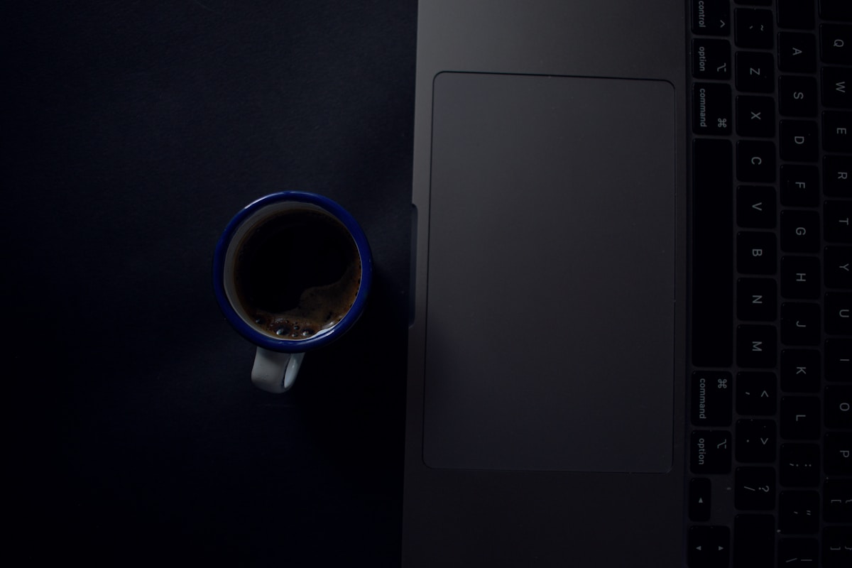 Cangkir kopi di sebelah laptop yang terbuka, ilustrasi risiko tumpahan cairan